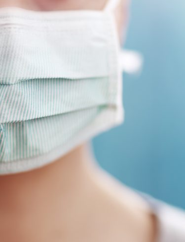 young woman in medical face protection mask indoors on blue background. Sick person